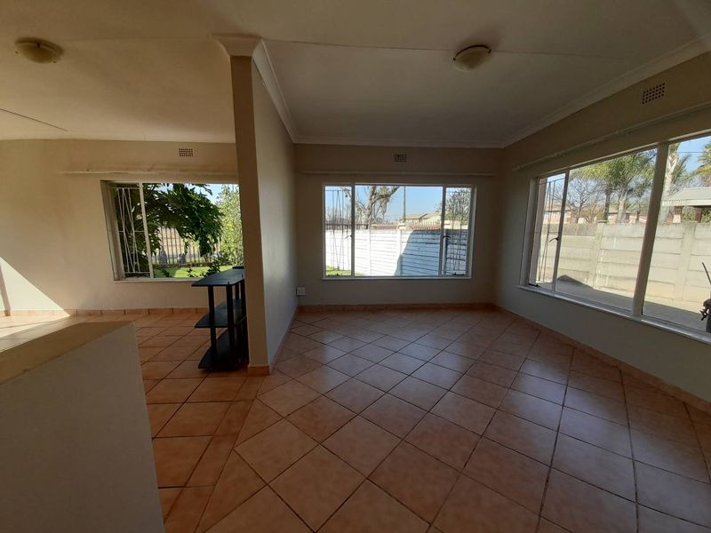 Spacious, light-filled living area featuring neutral ceramic tile flooring, coved cornicing, and large windows with security bars, offering a blank canvas for interior design.