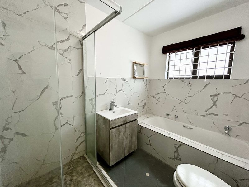 Modern bathroom featuring marble-look wall tiles, a glass shower enclosure, a built-in bathtub, and a vanity cabinet with a basin.