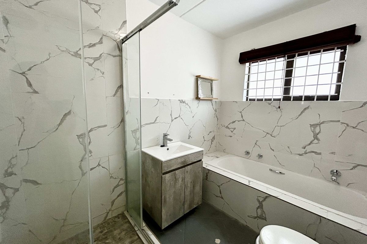 Modern bathroom featuring marble-look wall tiles, a glass shower enclosure, a built-in bathtub, and a vanity cabinet with a basin.