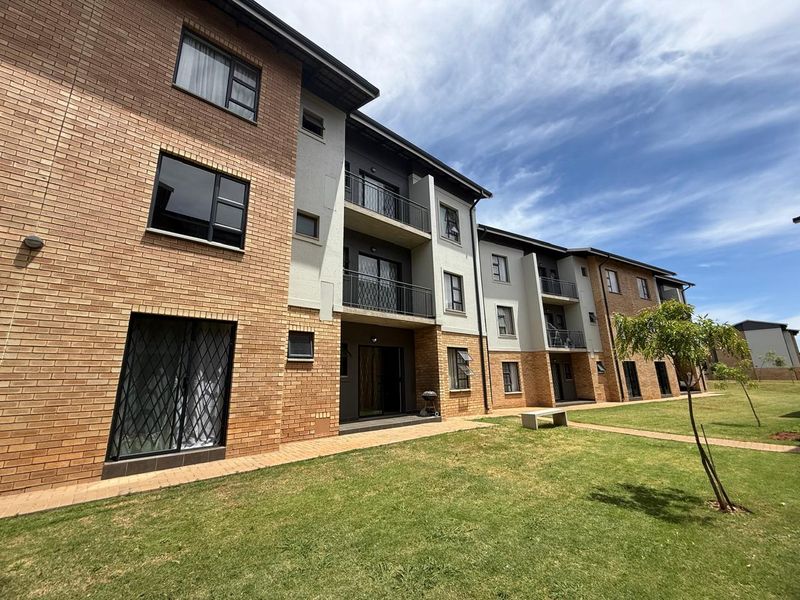 A view of the rear elevation of a multi-story apartment complex featuring face brick and plaster finishes, balconies with metal railings, and a communal lawn.