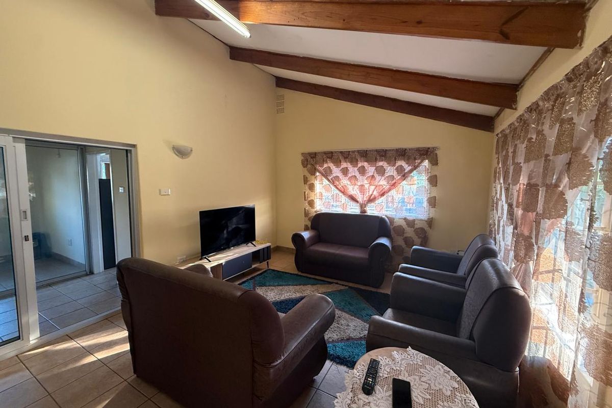 A living room featuring exposed timber ceiling beams, tiled flooring, and a sliding glass door providing access to the exterior.