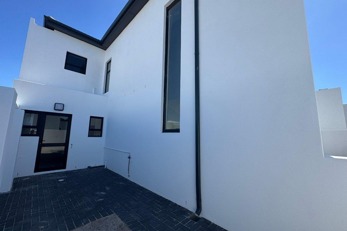 A modern exterior rear view of the property featuring clean white rendered walls, dark window frames, and paved outdoor area.