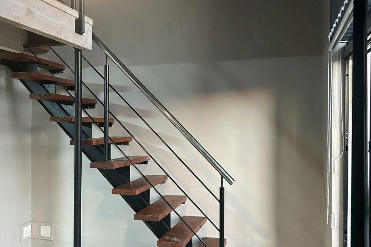 Modern open-plan living area featuring a stylish industrial-style staircase with wooden treads and metal railings leading to a mezzanine level.