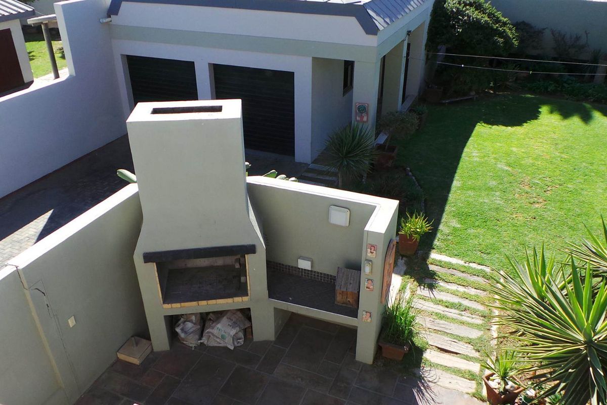 Aerial view of a backyard featuring a built-in masonry braai area with tiled patio, adjacent lawn, and detached garage structure.