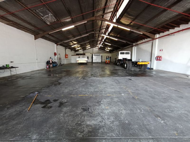 Spacious industrial warehouse or garage featuring high ceilings with exposed steel trusses, concrete flooring, and integrated fire safety systems.