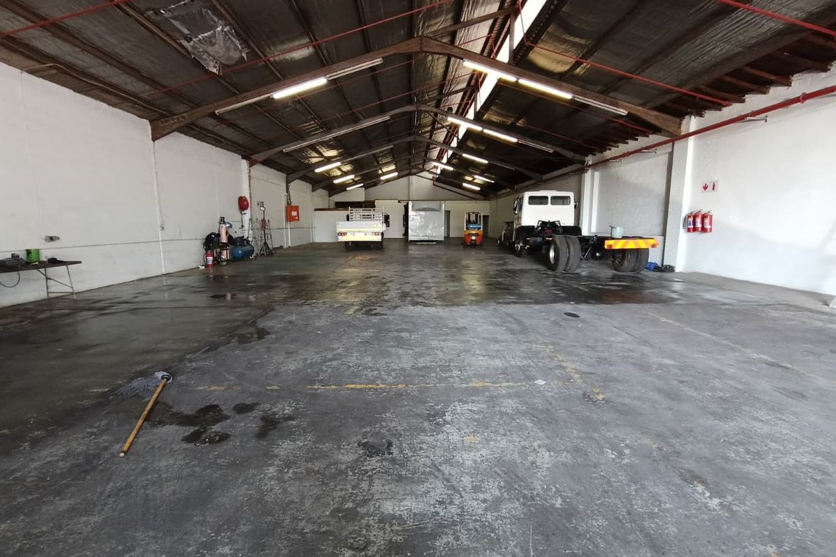 Spacious industrial warehouse or garage featuring high ceilings with exposed steel trusses, concrete flooring, and integrated fire safety systems.