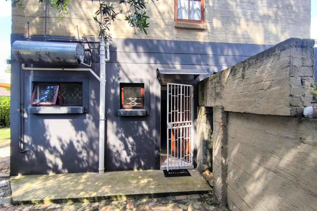 Rear exterior view of the property featuring a security gate entrance, external geyser unit, and concrete pathway adjacent to a boundary wall.
