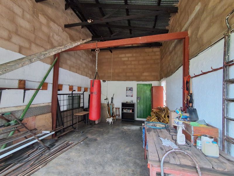 A functional utility or workshop space featuring exposed brick walls, concrete flooring, and steel roof trusses, suitable for storage or farm maintenance activities.
