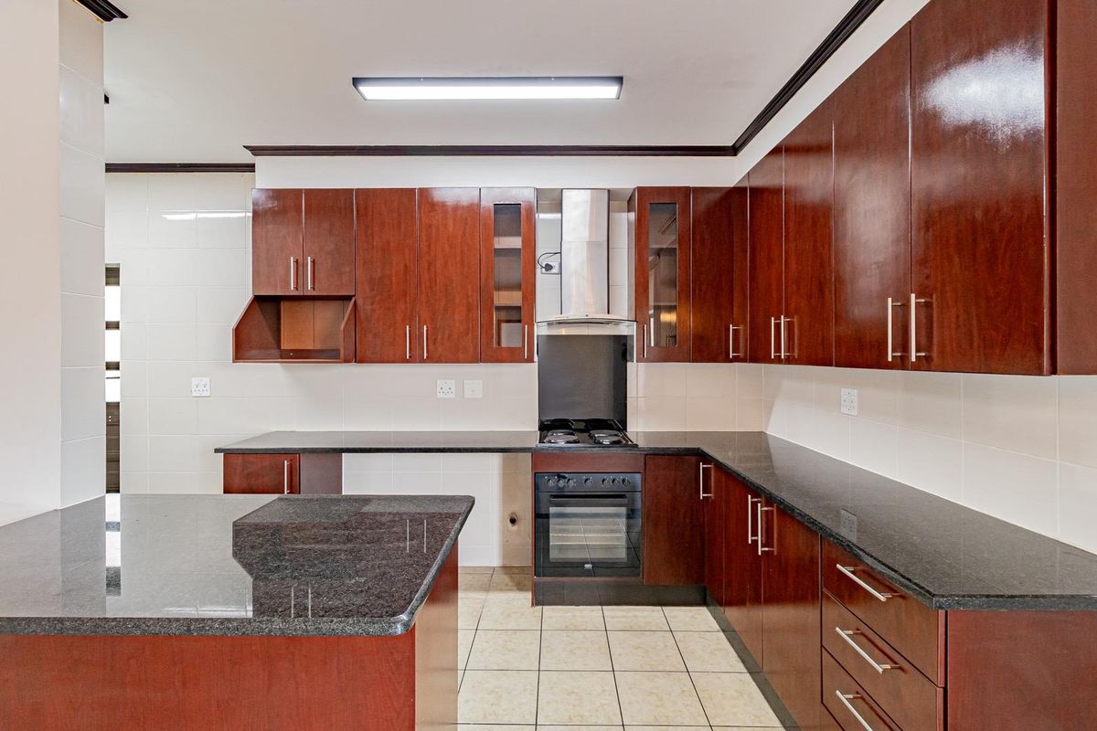 A functional kitchen featuring dark wood cabinetry, granite countertops, a built-in oven, gas hob, and stainless steel extractor fan.