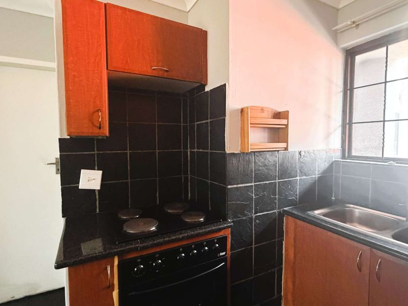 Compact kitchen featuring dark tiled splashbacks, built-in cabinetry, an electric hob with oven, and a double bowl sink.