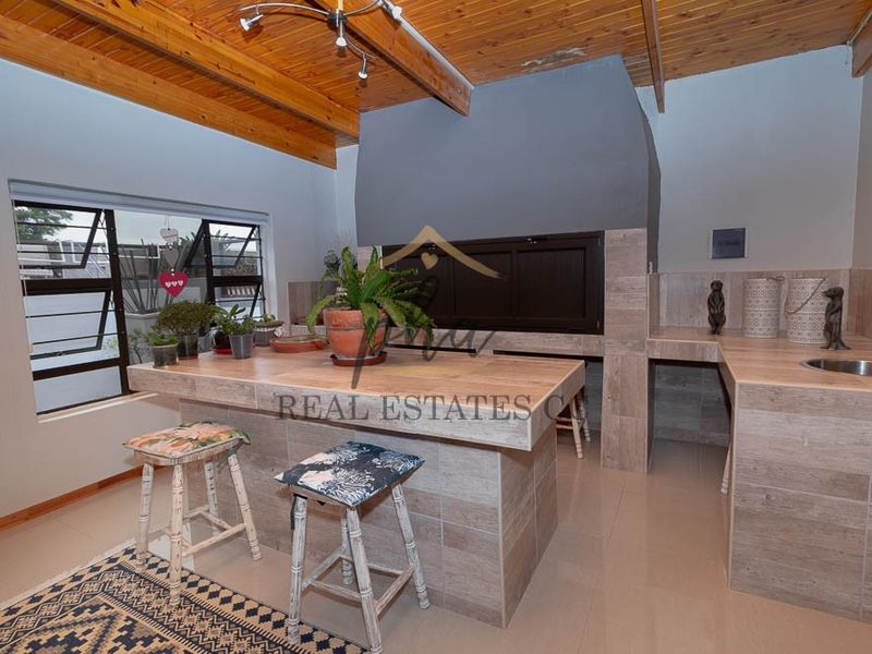 Covered patio area featuring a built-in braai, tiled island with sink, and exposed timber beam ceiling.