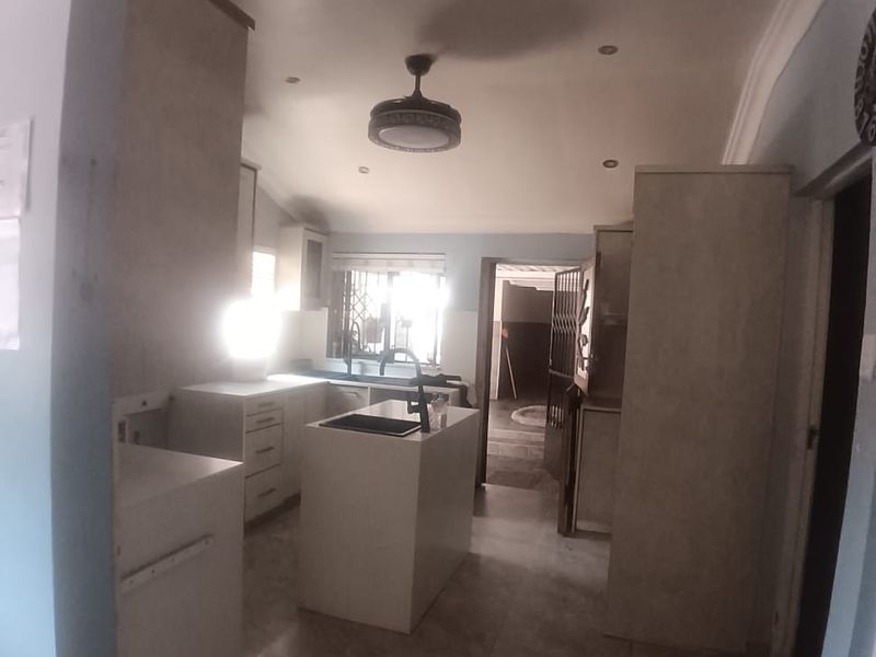 A functional kitchen space featuring a central island, built-in cabinetry, and tiled flooring, currently vacant and ready for personalization.