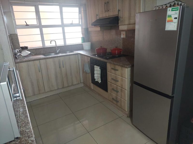 A functional kitchen featuring granite countertops, built-in cabinetry, a hob with extractor fan, and tiled flooring, offering a practical layout for daily use.