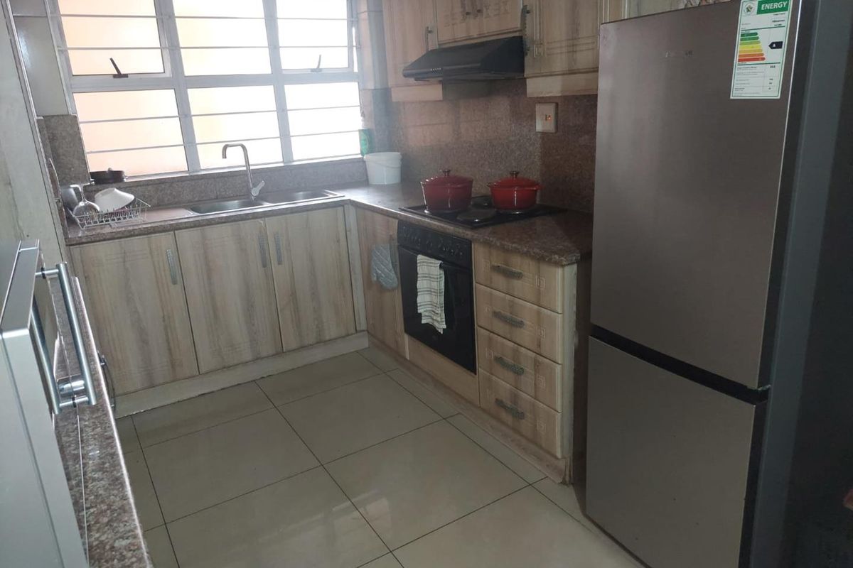 A functional kitchen featuring granite countertops, built-in cabinetry, a hob with extractor fan, and tiled flooring, offering a practical layout for daily use.