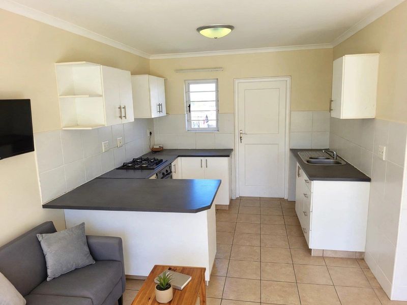 Open-plan kitchen and living area featuring white cabinetry, dark laminate countertops, gas hob, built-in oven, and tiled flooring throughout.