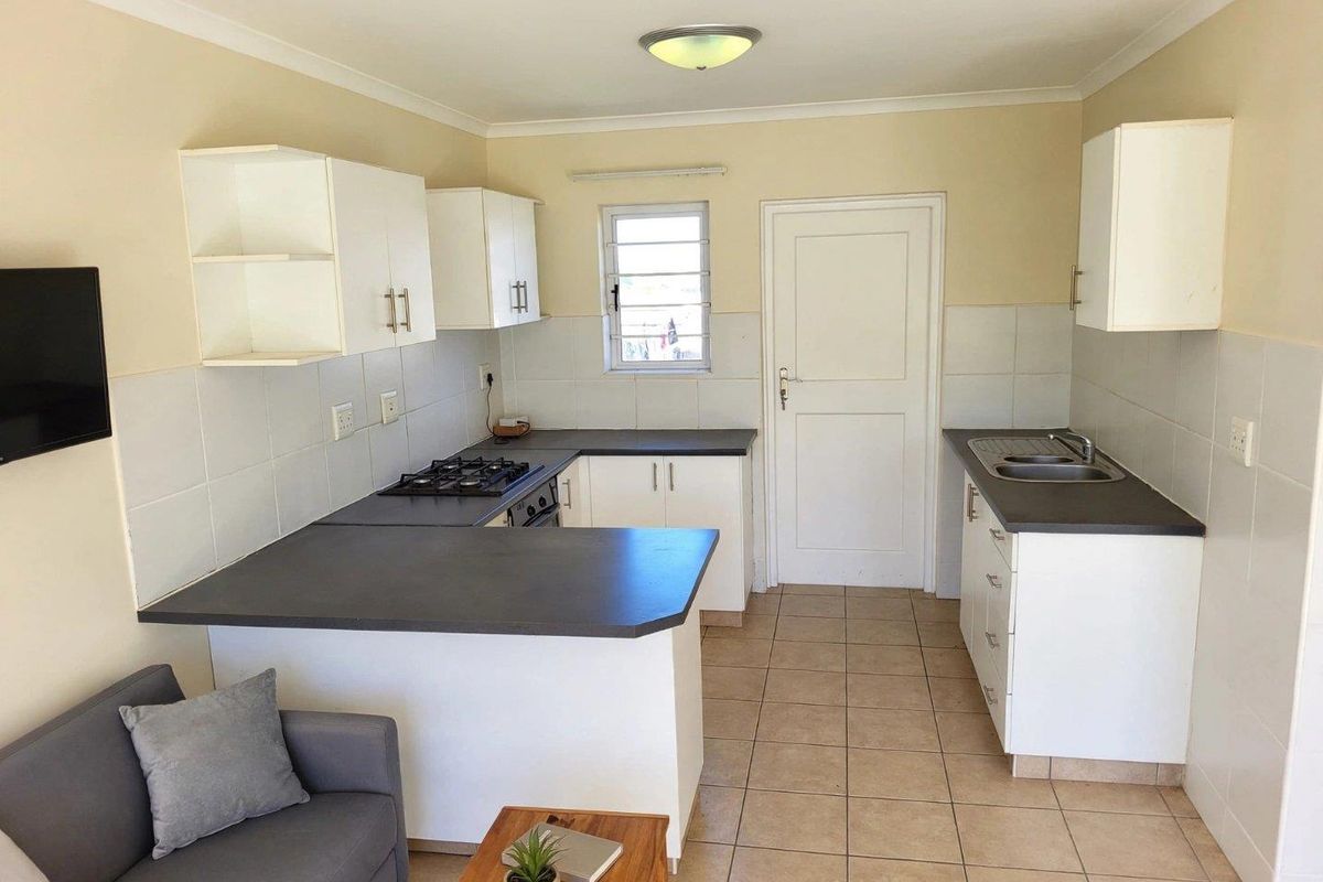 Open-plan kitchen and living area featuring white cabinetry, dark laminate countertops, gas hob, built-in oven, and tiled flooring throughout.