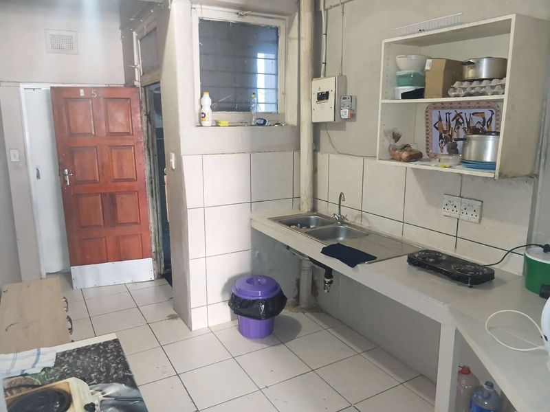 A functional kitchen area featuring a double basin sink, tiled splashback, and built-in shelving, requiring cosmetic updates to modernize the space.