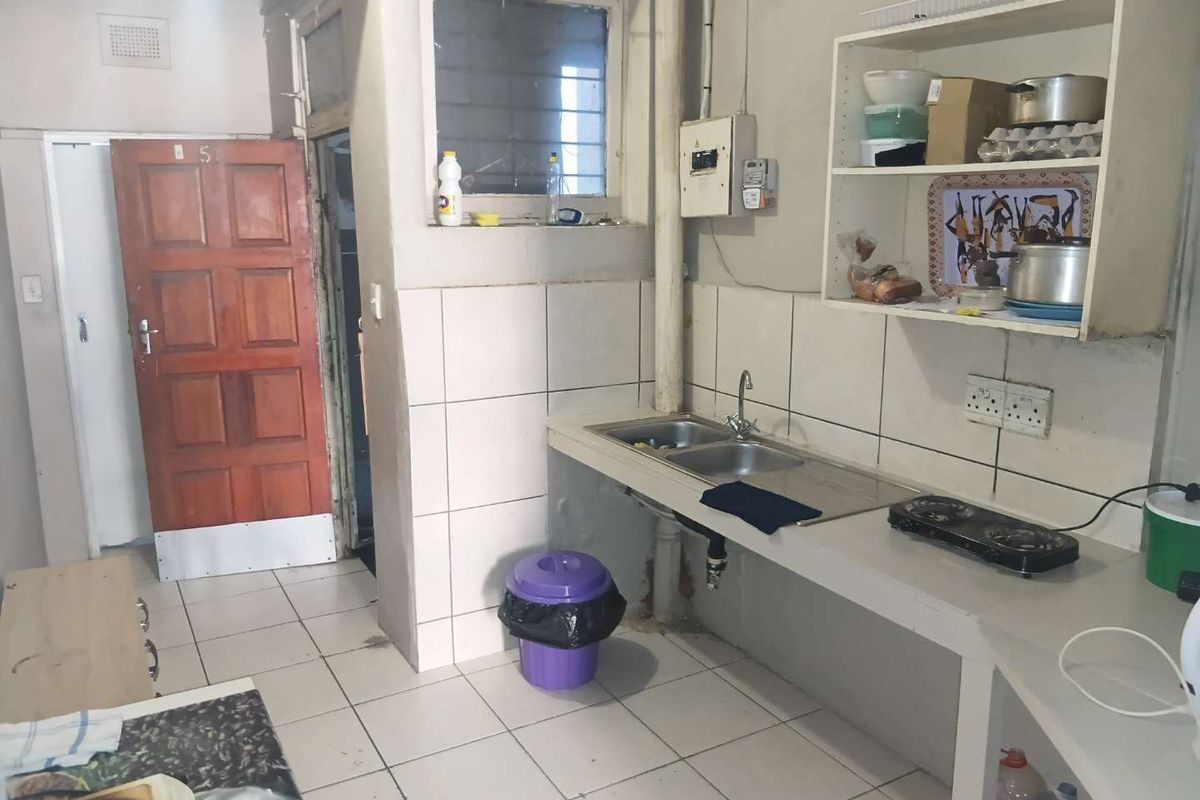 A functional kitchen area featuring a double basin sink, tiled splashback, and built-in shelving, requiring cosmetic updates to modernize the space.