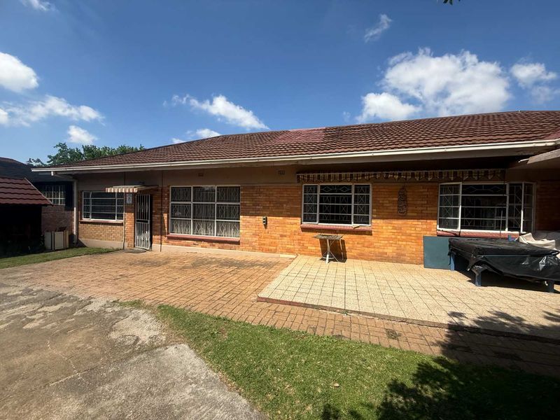 Rear view of a single-story brick house featuring a paved patio area, tiled roof, and security bars on the windows.