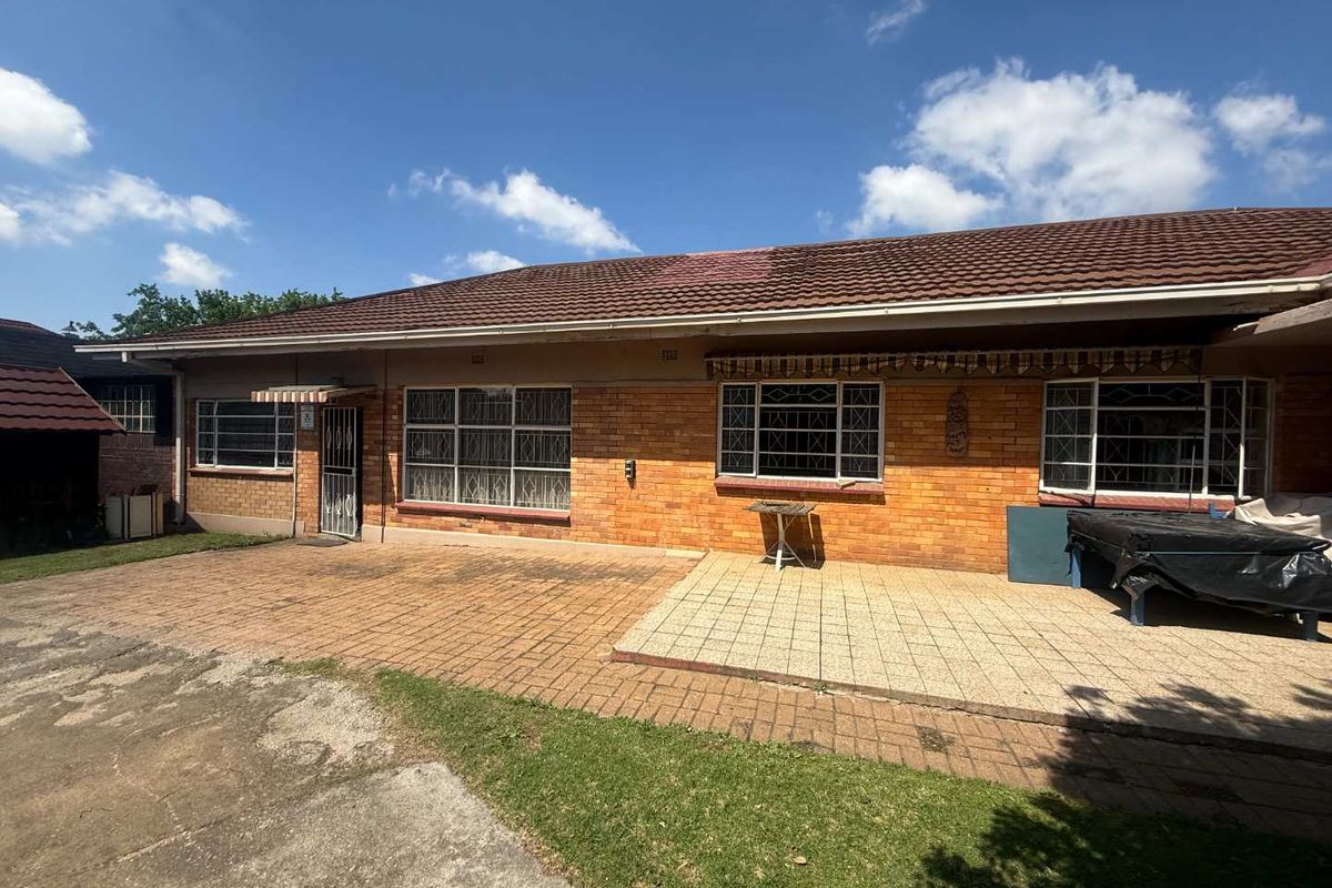 Rear view of a single-story brick house featuring a paved patio area, tiled roof, and security bars on the windows.
