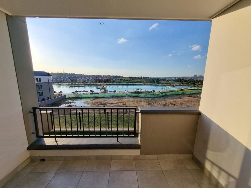 A covered balcony featuring tiled flooring and a metal balustrade, offering an expansive view over the surrounding landscape and water feature.
