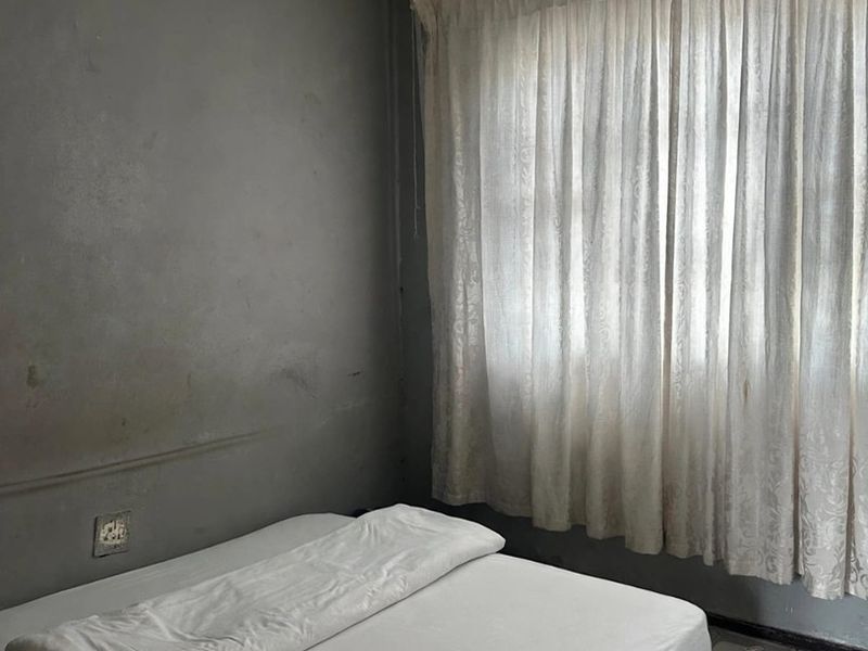 A bedroom featuring tiled flooring and significant signs of wear, including visible water damage on the ceiling and distressed wall finishes.