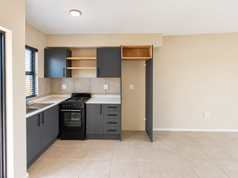 Modern kitchen featuring dark grey cabinetry, light countertops, a freestanding stove, and neutral tiled flooring in an open-plan layout.
