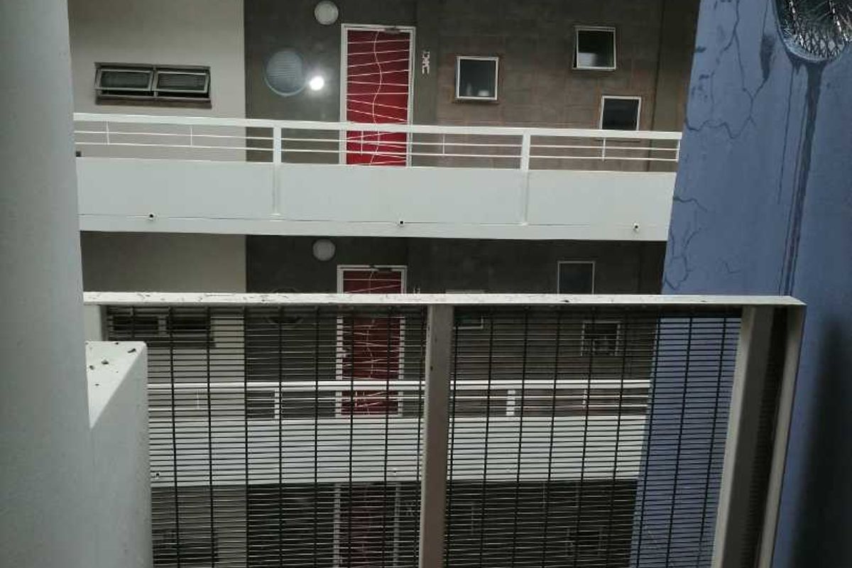 View of an apartment building exterior featuring a tiled balcony with metal balustrades and security gates.