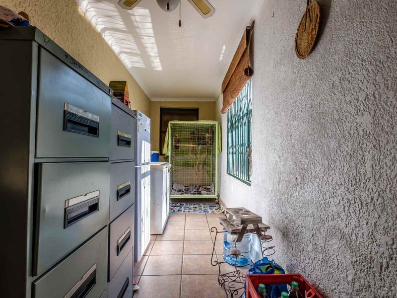 A functional utility space featuring tiled flooring, a ceiling fan, and security bars on the windows, suitable for storage or laundry use.
