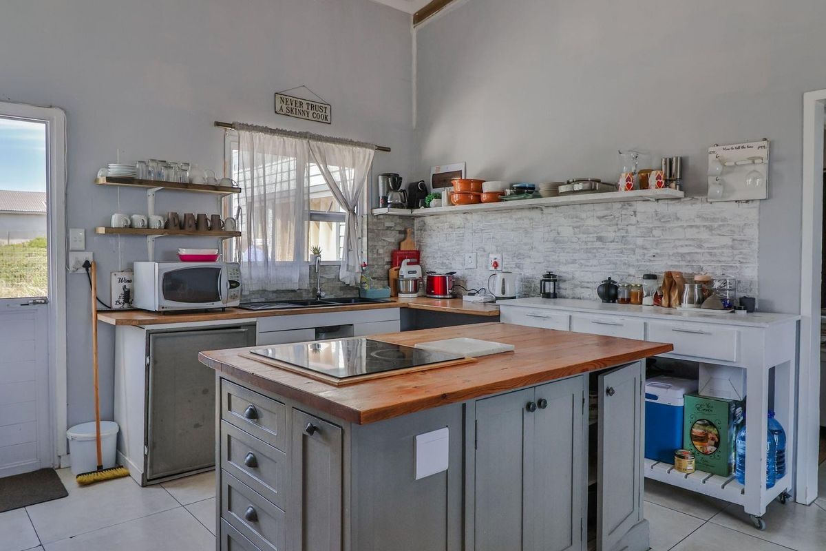 A functional kitchen featuring a central wooden island with a built-in cooktop, open shelving, and tiled flooring with direct access to the exterior.