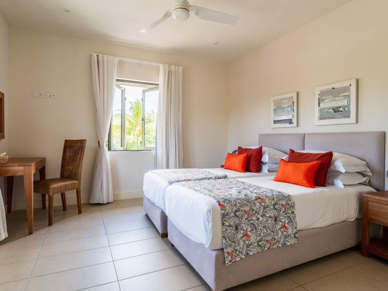 A bright and airy bedroom featuring neutral tiled flooring, a ceiling fan, and a window providing natural light and garden views.