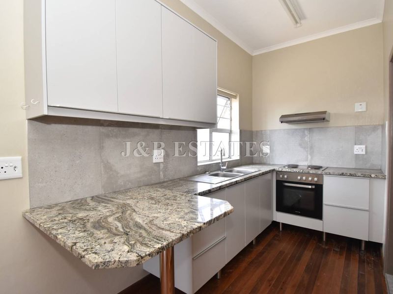 A functional kitchen featuring granite countertops, built-in oven, hob, extractor fan, and ample cabinetry with a double sink.