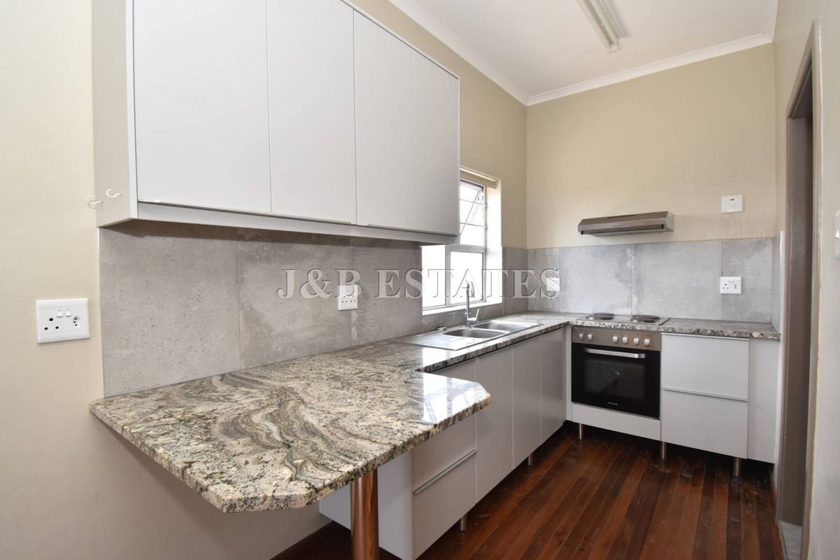 A functional kitchen featuring granite countertops, built-in oven, hob, extractor fan, and ample cabinetry with a double sink.