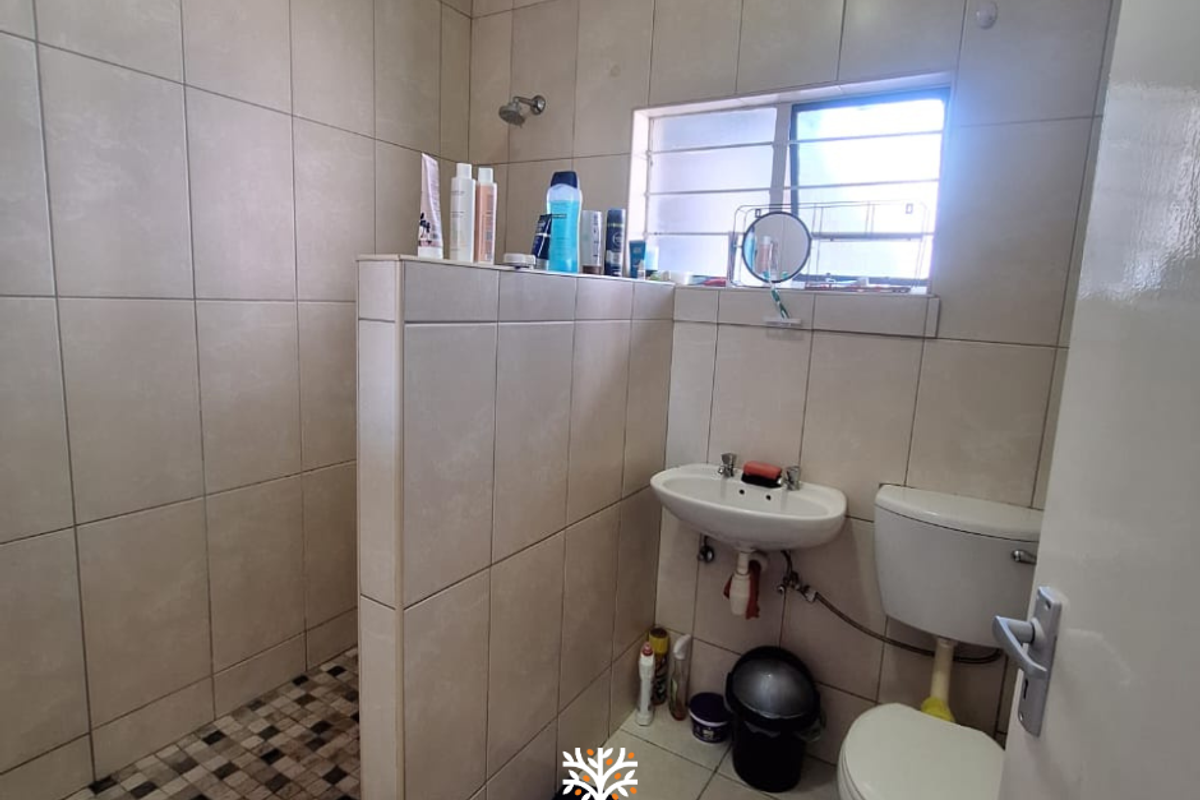 A functional bathroom featuring a walk-in shower with mosaic floor tiles, a wall-mounted basin, and a standard toilet.