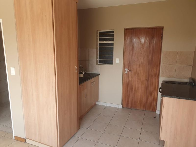 A compact kitchen area featuring built-in wooden cabinetry, laminate countertops, a stainless steel sink, and tiled flooring in a neutral, functional layout.