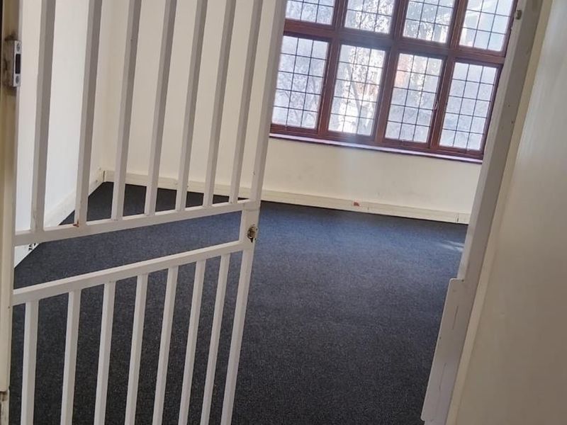 An empty office space featuring dark carpeting, large leaded glass windows, and a white security gate at the entrance.