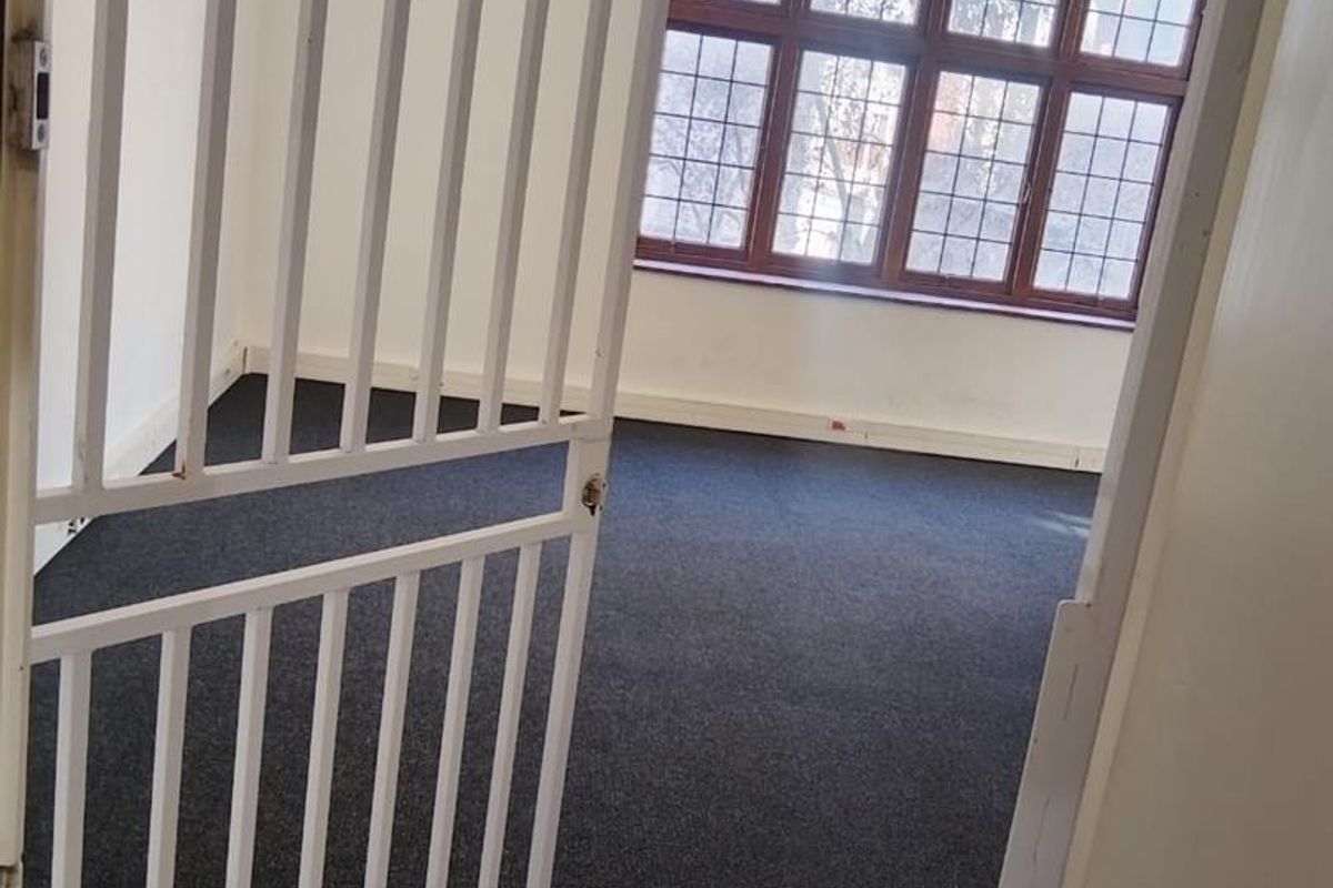 An empty office space featuring dark carpeting, large leaded glass windows, and a white security gate at the entrance.