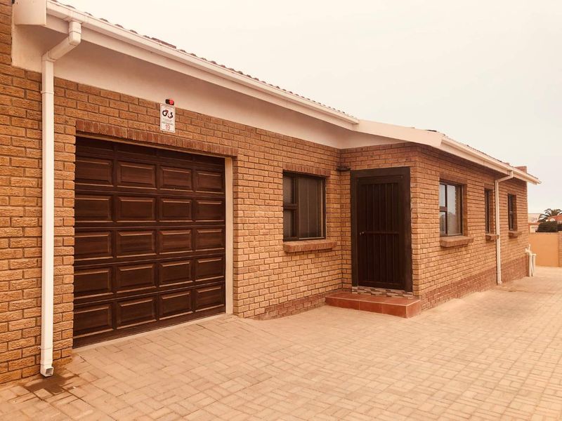 Front exterior view of a townhouse featuring a face brick facade, paved driveway, and a secure garage entrance.