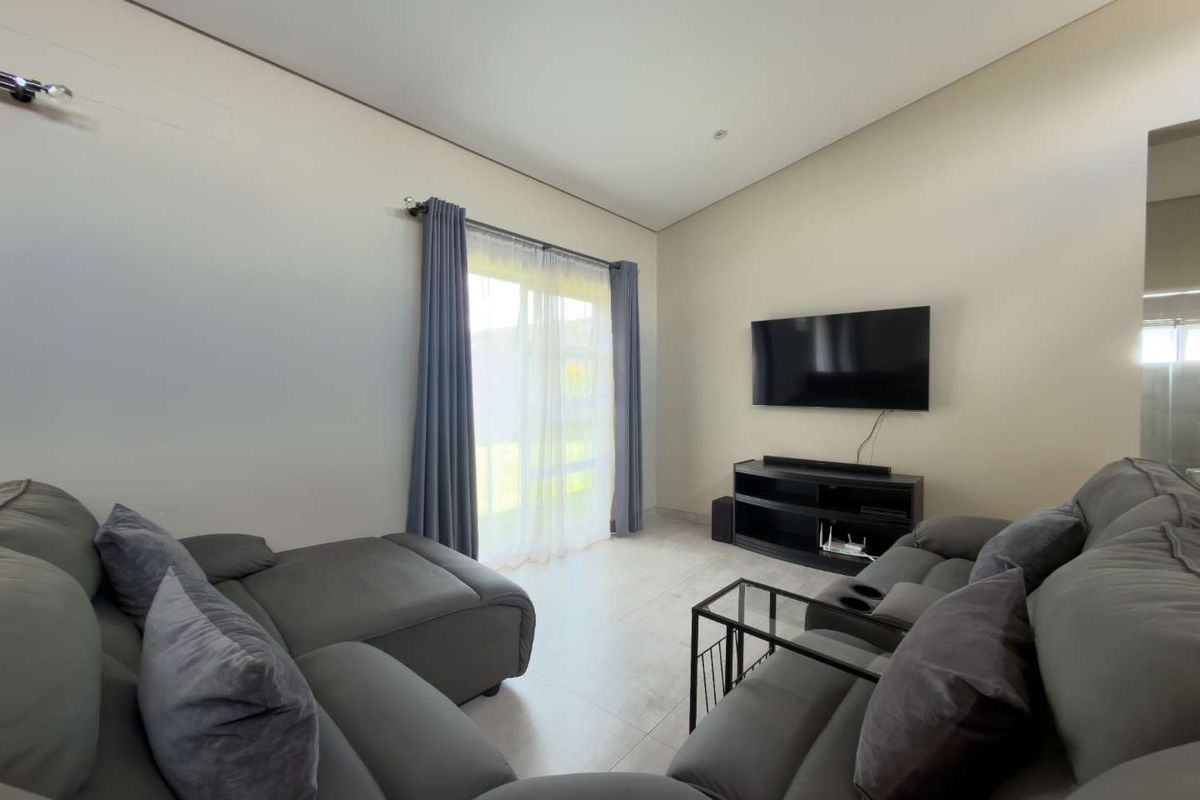 A bright living room featuring neutral tiled flooring, high ceilings, and a large sliding glass door providing natural light and access to the outdoors.