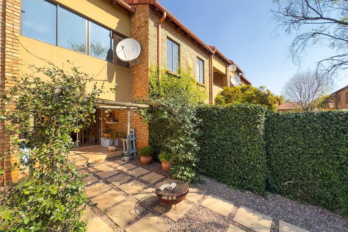 Rear exterior view of the townhouse featuring a paved patio area, brick facade, and established garden landscaping.