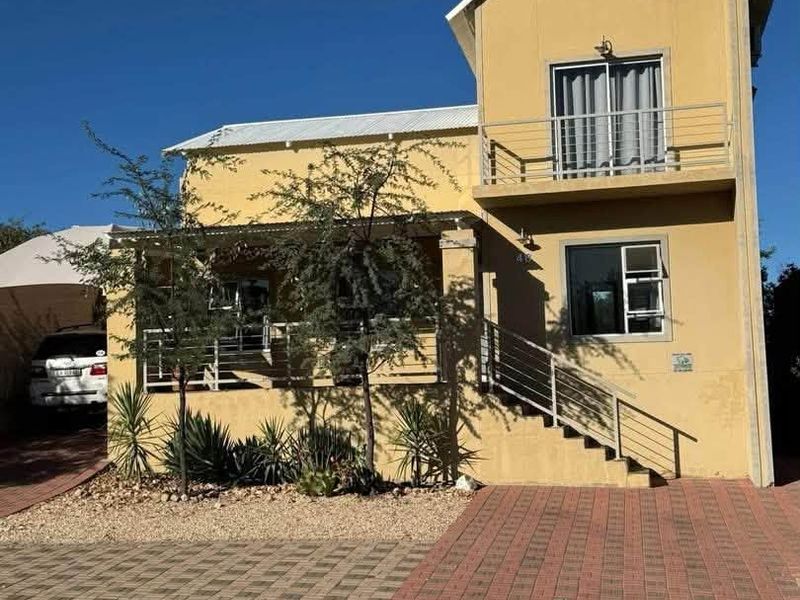 Front elevation of a two-story house featuring a paved driveway, a covered patio, and an upper-level balcony with metal railings.