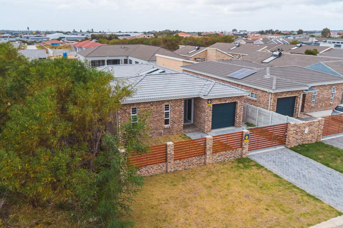 Aerial view of a modern brick-faced residential property featuring a tiled roof, integrated garage, paved driveway, and secure perimeter fencing.