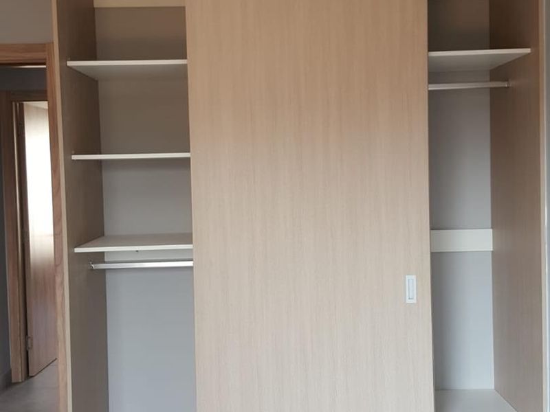 A bedroom featuring a modern, light wood-finish built-in wardrobe with sliding doors, internal shelving, and hanging rails.