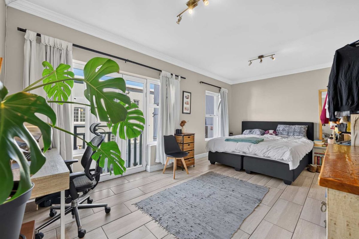 Spacious bedroom featuring tiled flooring, crown molding, and direct access to a balcony through double glass doors, providing ample natural light.