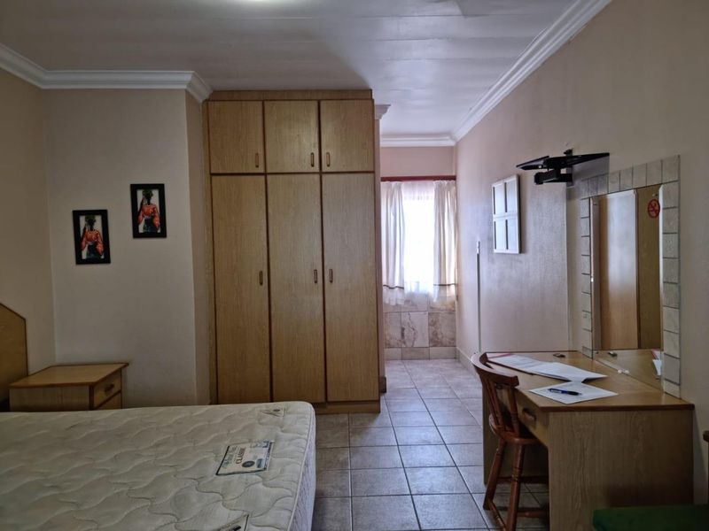 A bedroom featuring tiled flooring, a built-in wooden wardrobe, and a vanity area with a mirror.