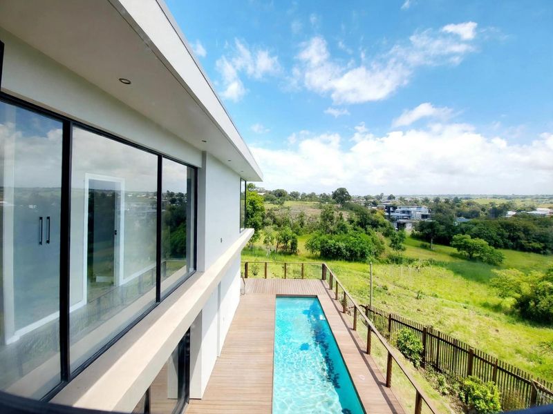 Modern exterior view featuring a lap pool with timber decking, glass sliding doors, and expansive views of the surrounding landscape.
