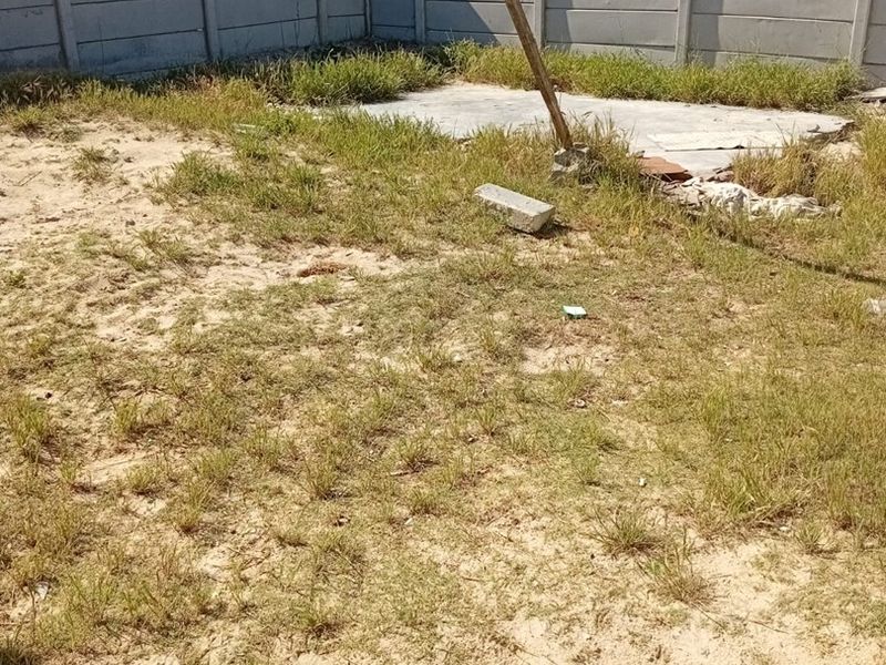 A backyard area featuring a precast concrete boundary wall and a small concrete slab, currently requiring landscaping and site clearing.