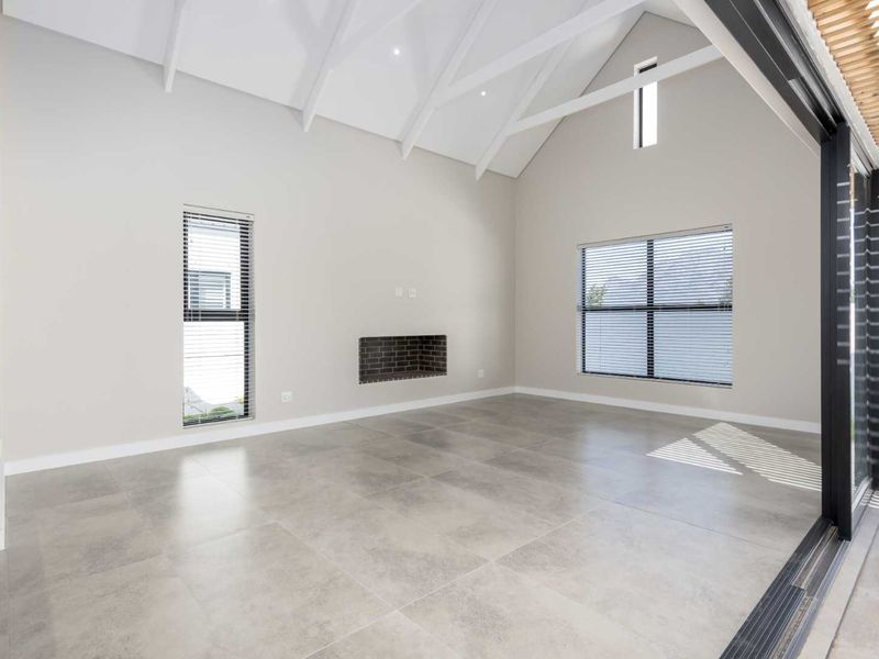 Spacious living area featuring a high vaulted ceiling with exposed rafters, large format floor tiles, a built-in fireplace, and seamless access to the outdoors.