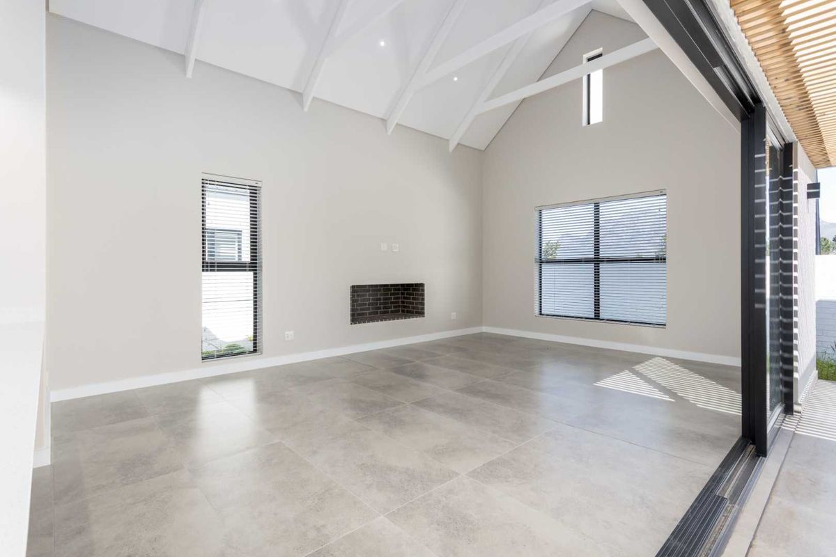 Spacious living area featuring a high vaulted ceiling with exposed rafters, large format floor tiles, a built-in fireplace, and seamless access to the outdoors.