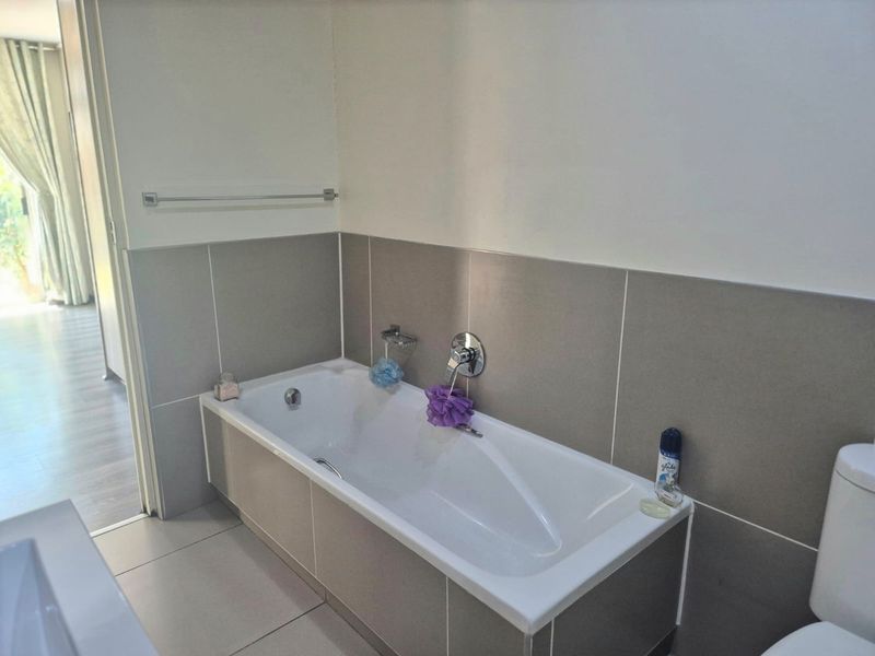 A clean, modern bathroom featuring a built-in bathtub with chrome fixtures, neutral wall tiling, and tiled flooring.